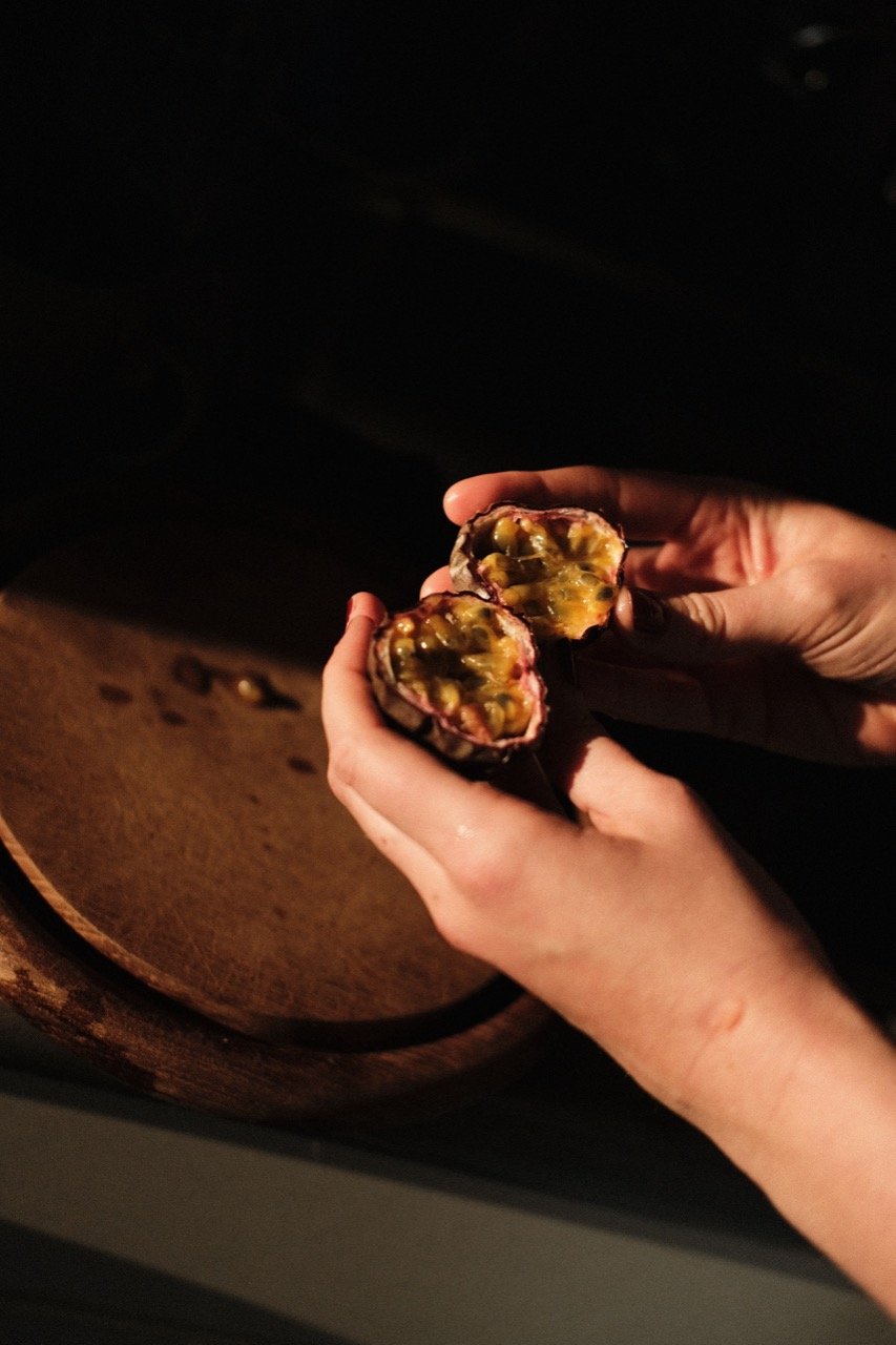 Hands holding a cut passionfruit in warm light.