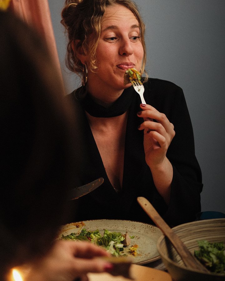 Woman enjoying a shared meal at a table with salad and warm light.